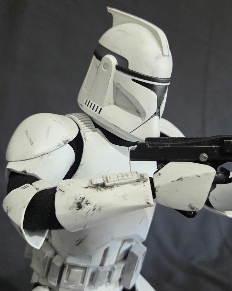May include: A white and black Clone Trooper helmet and armor, with a blaster rifle. The armor has black accents and visible wear and tear. The helmet has a distinctive design with a visor and antenna.