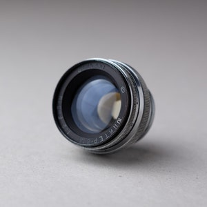 May include: A silver and black camera lens with the text "Jupiter-8" and "T.E.P. 58 mm 1:2" printed on the side.