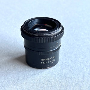 Puede incluir: Un objetivo de cámara negro con el texto "KORREKTAR 1.6.3 F=150" impreso en el lateral.