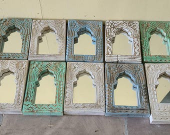 May include: A collection of ten small, rectangular mirrors with arched tops. The wooden frames are intricately carved and painted in shades of white, teal, and green. The mirrors are arranged on a stone surface.