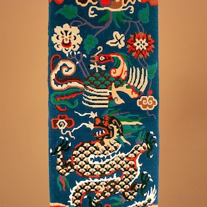 May include: A blue and red tapestry with a dragon and a phoenix on a blue background. The tapestry has a fringe border.