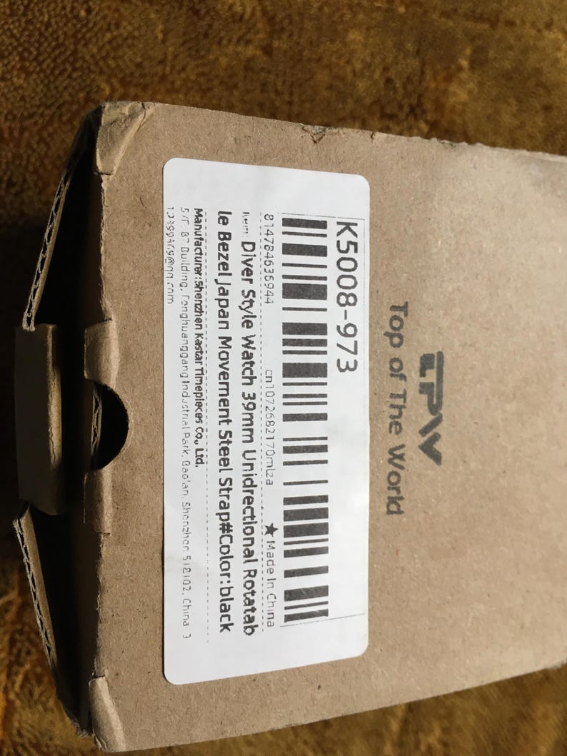 May include: A cardboard box with a label that reads "Diver Style Watch 39mm Unidirectional Rotatab" and "K5008-973". The label also includes the text "Top of The World" and a barcode. The watch strap color is black.