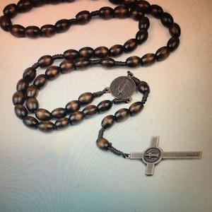 May include: A brown wooden rosary with a metal cross and a medal featuring a saint. The rosary beads are oval shaped and the cross is a simple design.