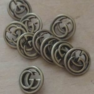 Könnte beinhalten: Eine Gruppe von zehn goldfarbenen Metallknöpfen mit dem doppelten G-Logo des italienischen Luxusmodehauses Gucci.