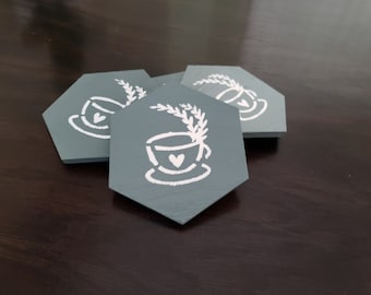 May include: Three gray hexagonal coasters with a white design of a teacup with a heart and a sprig of leaves.