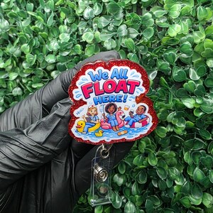 May include: A red glitter badge reel with the text "We All FLOAT HERE!" and an illustration of people floating on pool floats. The badge reel has a clear plastic strap and a metal clip.
