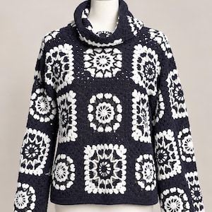 Könnte beinhalten: Ein langärmeliger Pullover mit Wasserfallkragen, der aus einer Reihe von dunkel marineblauen und weißen gehäkelten Granny Squares besteht. Das Kleidungsstück zeigt ein sich wiederholendes geometrisches Blumenmuster.