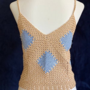 Puede incluir: Un top de crochet dorado con parches de mezclilla azul. El top tiene cuello en V y tirantes finos.