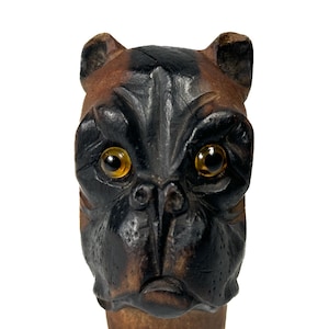 Peut inclure: Gros plan sur une tête de chien en bois avec une fourrure noire et brune et des yeux en verre ambre. La gueule du chien est légèrement ouverte, révélant ses dents.
