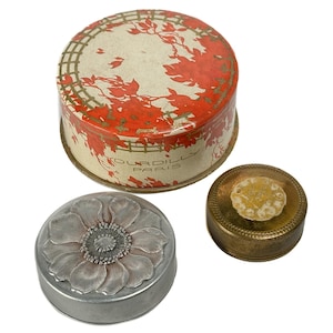 Può includere: Tre scatole decorative antiche. La più grande è rotonda con un motivo floreale rosso e bianco e la scritta "TOURDILLY PARIS". Una scatola color argento ha la forma di un fiore. È presente anche una piccola scatola rotonda color ottone.