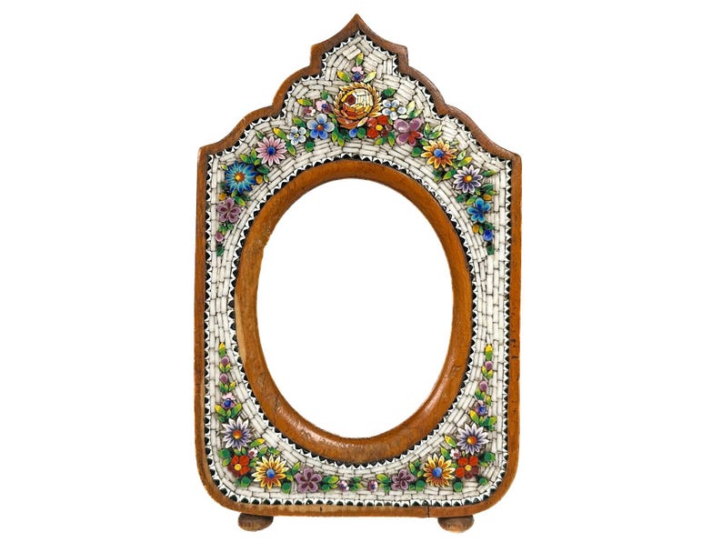 May include: Wooden picture frame with an oval aperture. The frame is decorated with a mosaic of small white tiles and colourful flowers. The frame has a decorative top and small feet.