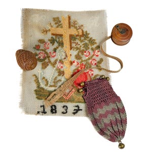 Pode incluir: Um mostruário de bordado retangular com um design de cruz e flores com o ano 1837, acompanhado por um pequeno objeto de madeira esculpida, uma fita métrica redonda de madeira com fita de tecido e uma bolsa de crochê em malva e prata.