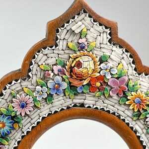 May include: A decorative wooden frame with a mosaic floral design. The mosaic features colourful flowers in shades of pink, blue, yellow, and orange, set against a white background. The frame has a brown border.