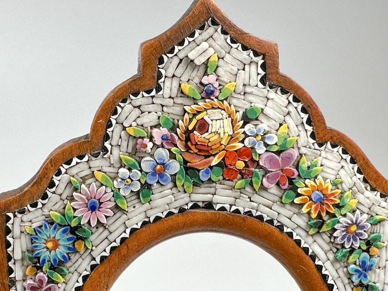 May include: A decorative wooden frame with a mosaic floral design. The mosaic features colourful flowers in shades of pink, blue, yellow, and orange, set against a white background. The frame has a brown border.