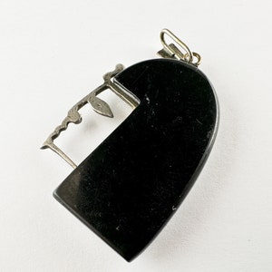 Puede incluir: Un colgante de coraz&oacute;n negro con un dise&ntilde;o de filigrana plateada. El colgante tiene una abertura con bisagra y un peque&ntilde;o bucle en la parte superior para sujetar una cadena.