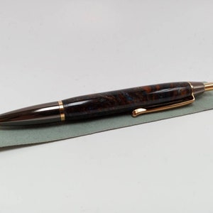 May include: A brown and gold pen with a marbled design. The pen is lying on a gray surface.