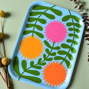 Puede incluir: Una bandeja azul con un diseño floral. La bandeja presenta hojas verdes y tres flores en tonos naranja, rosa y amarillo.