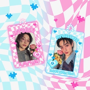 Puede incluir: Dos colgantes fotográficos rectangulares con imágenes de personas, enmarcados en rosa y azul. El colgante rosa dice "MY BIAS" y "I LOVE THEM!" El colgante azul dice "MY WRECKER" y "I LOVE THEM TOO!" El fondo es un patrón de cuadros.