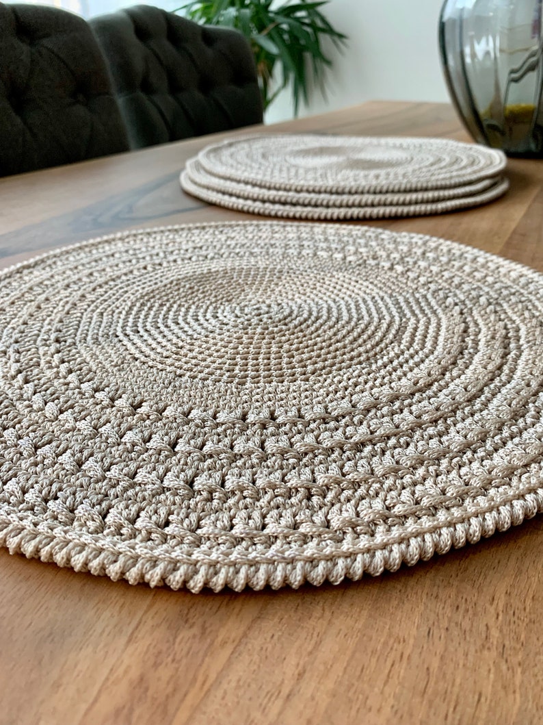 May include: A set of three beige crocheted placemats on a wooden table. The placemats are round and have a textured design.