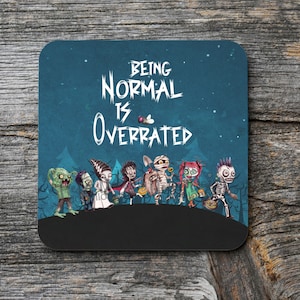 May include: A blue and black coaster with the text "Being Normal Is Overrated" in white. A group of cartoon monsters dressed in Halloween costumes are walking across the bottom of the coaster.