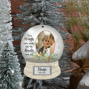 May include: A white snow globe ornament with a photo of two women inside. The globe has a wooden base with the text "Nana 1948-2012" on it. The text on the globe reads "Your wings were ready but our hearts were not."