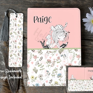 May include: A pink personalized notebook cover with a floral design and a girl reading a book with cats on her head. The name "Paige" is printed on the cover. A matching bookmark with a floral design is included.