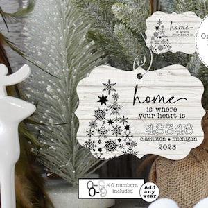 Puede incluir: Adorno de madera blanco con un diseño de copo de nieve negro y el texto "home is where your heart is 48346 clarkston michigan 2023".