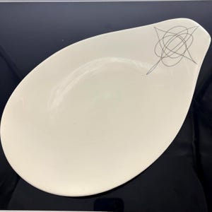 May include: Cream-colored, oval-shaped serving dish with a slightly raised rim. A gray abstract design is on the upper right side. The dish has a smooth, glossy finish and is suitable for serving appetizers or side dishes.