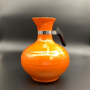 May include: Orange ceramic pitcher with a black handle and a silver band around the neck.