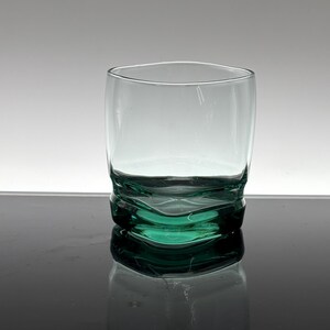 Pu&ograve; includere: Un bicchiere trasparente soffiato a mano con una base strutturata unica di colore verde acqua intenso. Il bicchiere ha una forma arrotondata e una parte superiore liscia e trasparente. La base presenta un design ondulato e organico. Adatto alle bevande.