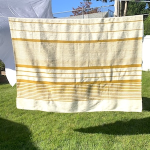 May include: A white and yellow striped throw blanket hanging on a clothesline. The blanket has a textured, fuzzy surface.