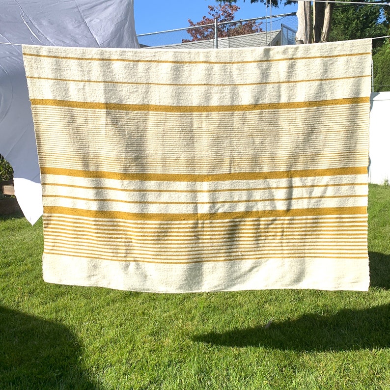 May include: A white and yellow striped throw blanket hanging on a clothesline. The blanket has a textured, fuzzy surface.