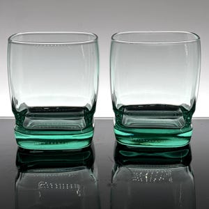 Pu&ograve; includere: Due bicchieri trasparenti di forma quadrata con una base color verde acqua. I bicchieri hanno una base spessa e robusta e un design semplice ed elegante. I bicchieri vengono probabilmente utilizzati per servire bevande.