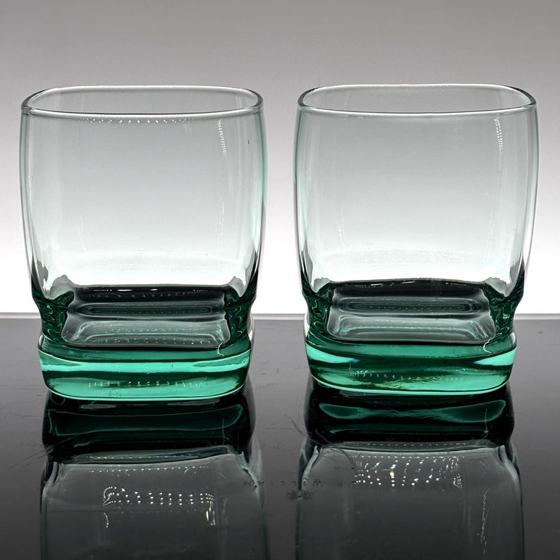 Pu&ograve; includere: Due bicchieri trasparenti di forma quadrata con una base color verde acqua. I bicchieri hanno una base spessa e robusta e un design semplice ed elegante. I bicchieri vengono probabilmente utilizzati per servire bevande.