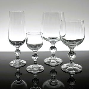 May include: Four clear glass drinking glasses with a decorative, faceted, ball-shaped stem. The glasses are arranged in a row on a black surface.