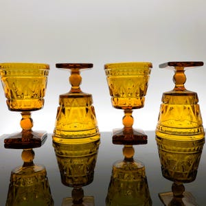May include: Four amber glass goblets with a diamond pattern. The goblets have a square base and a round bowl.