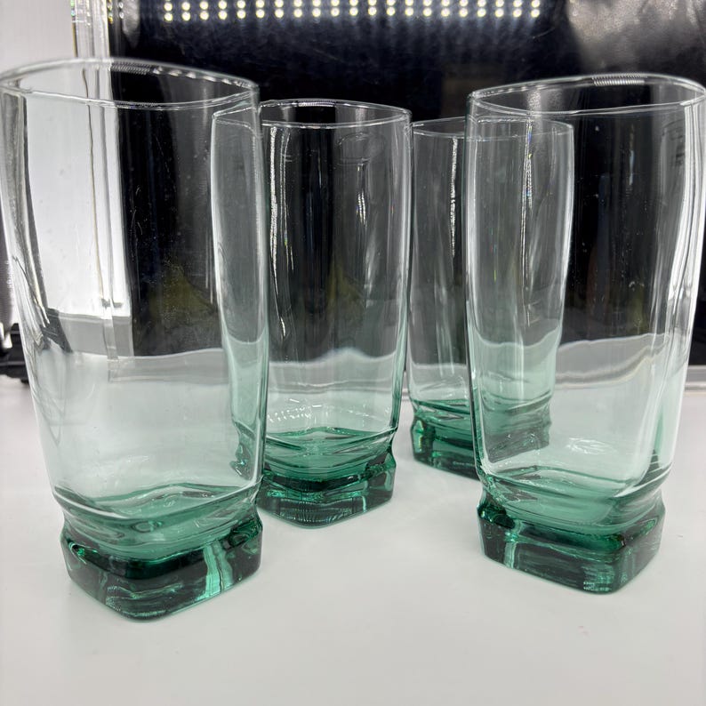 Pu&ograve; includere: Set di quattro bicchieri trasparenti con una leggera sfumatura verde. I bicchieri hanno una base rettangolare e una forma cilindrica alta. Il vetro &egrave; spesso e robusto, adatto all'uso quotidiano. Altezza: circa 15 cm.