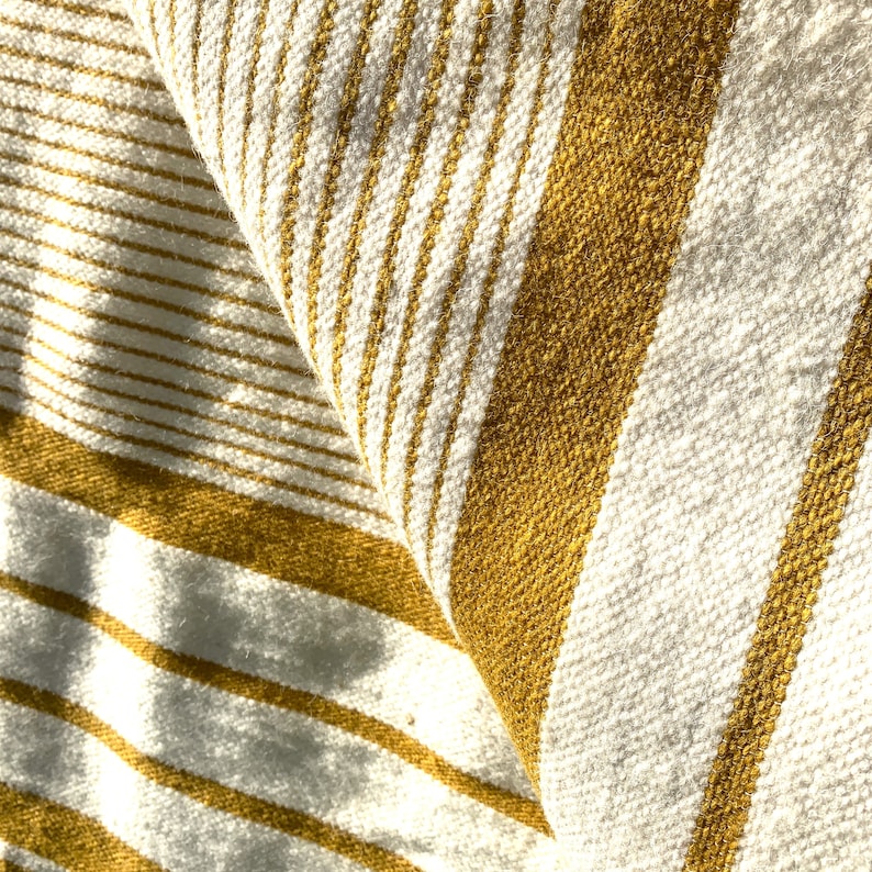 May include: Close-up of a white and mustard yellow striped fabric. The fabric is woven with a textured pattern and has a soft, cozy feel.