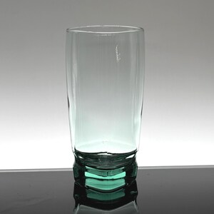 Pu&ograve; includere: Un bicchiere alto e trasparente con una leggera sfumatura verde. Il bicchiere ha una forma cilindrica e una base geometrica. Il bicchiere vuoto sembra essere fatto di un materiale spesso e resistente.