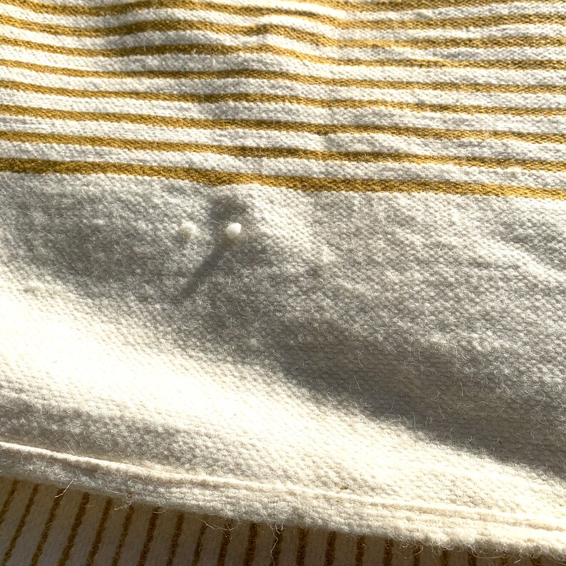 May include: Close-up of a white and mustard yellow striped throw blanket with a textured weave. The blanket is folded and has a slight sheen.