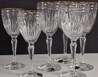 Könnte beinhalten: Ein Set aus klaren Kristall-Weingläsern mit Goldrändern. Die Gläser haben ein geripptes Design auf der Schale und einen facettierten Stiel. Die Gläser stehen auf einer weißen Oberfläche vor dunklem Hintergrund.
