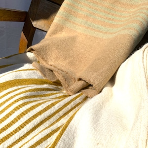 May include: Two striped blankets, one with white and yellow stripes and the other with beige and green stripes, are draped over a wooden chair.