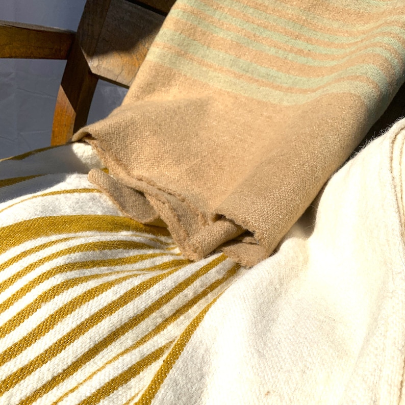May include: Two striped blankets, one with white and yellow stripes and the other with beige and green stripes, are draped over a wooden chair.