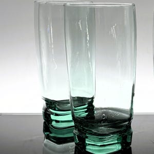 Pu&ograve; includere: Due alti bicchieri trasparenti con una leggera sfumatura verde. Le basi dei bicchieri presentano un design strutturato e stratificato, che aggiunge interesse visivo. Ideali per servire acqua, succo o altre bevande. Altezza circa 20 cm.