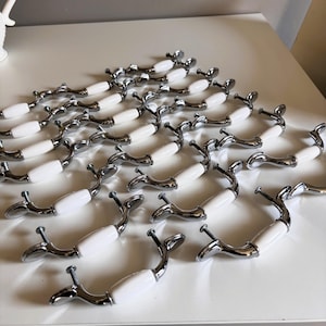 May include: A collection of cabinet pulls with a white ceramic center and chrome-finished metal handles. The pulls are arranged on a white surface, showcasing their curved design and screw attachments. These decorative hardware pieces are suitable for furniture restoration or new builds.