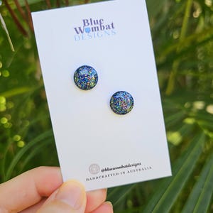 May include: A pair of small, round, blue glitter stud earrings on a white card with the text "Blue Wombat Designs" and "@bluewombatdesigns HANDCRAFTED IN AUSTRALIA".
