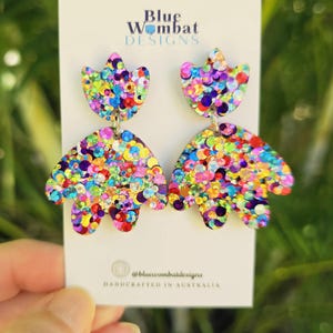 May include: Glittery, multi-coloured earrings in a floral design. The earrings are made by Blue Wombat Designs and handcrafted in Australia. The earrings have a top flower shape and a larger, petal-like bottom shape.