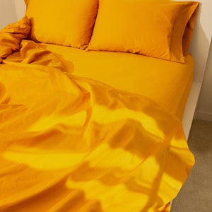 May include: A bed with bright yellow bedding. Two matching pillowcases rest on the bed, with a fitted sheet and a top sheet. The sheets are slightly rumpled, and the bed frame is white.