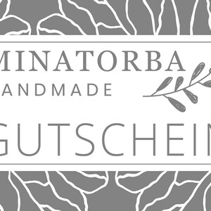 May include: A white rectangular gift certificate with a gray floral background. The text "MINATORBA HANDMADE GUTSCHEIN" is printed in white on the certificate.