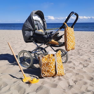 May include: A gray stroller with a black handle and wheels, a yellow tote bag with a white pattern, and a yellow beach shovel on a sandy beach.